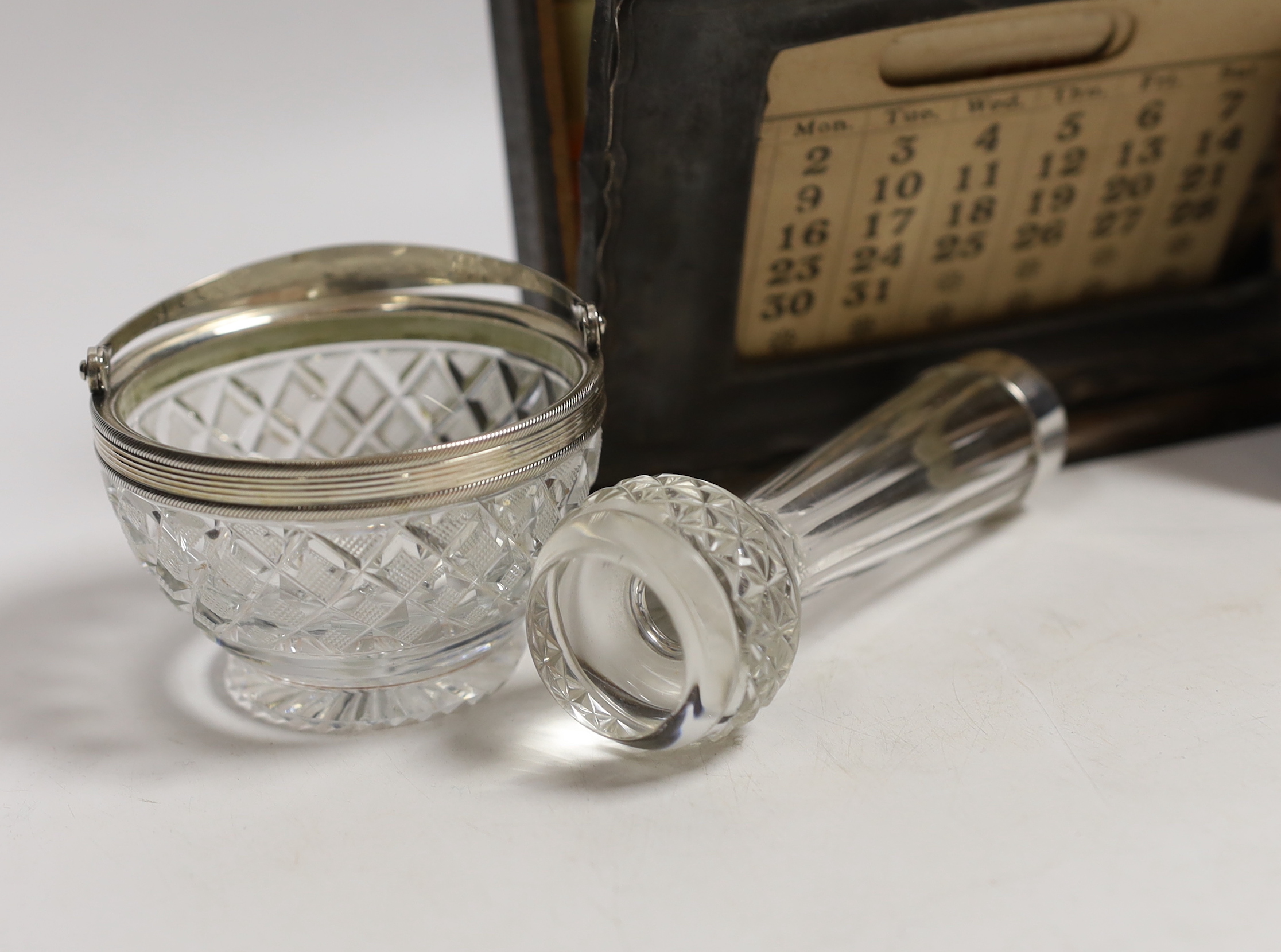 A pair of Edwardian silver knife rests, William Hutton & Sons, London, 1908, 77mm, a silver mounted wooden desk calendar, a late Victorian small silver mounted photograph frame, a silver mounted glass posy vase and a whi